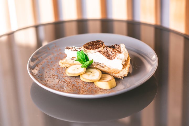 Kawałek ciasta banoffee z bitą śmietaną, kakao, plasterkami banana i miętą