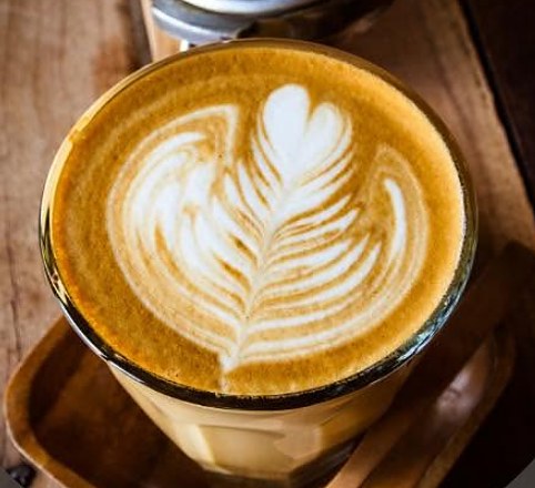 Kawa z latte art w szklance na drewnianej tacy